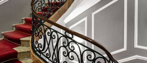Un escalier en colimaçon avec des marches recouvertes d’une moquette rouge et des rampes en métal noir à motifs.