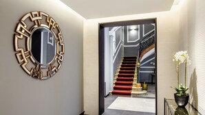 Un couloir moderne agrémenté d’un miroir aux motifs géométriques, d’un escalier recouvert d’une moquette rouge et d’une plante en pot.