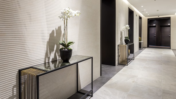 Un couloir moderne avec un mur texturé, une console en verre surmontée d’une orchidée en pot et un sol carrelé.