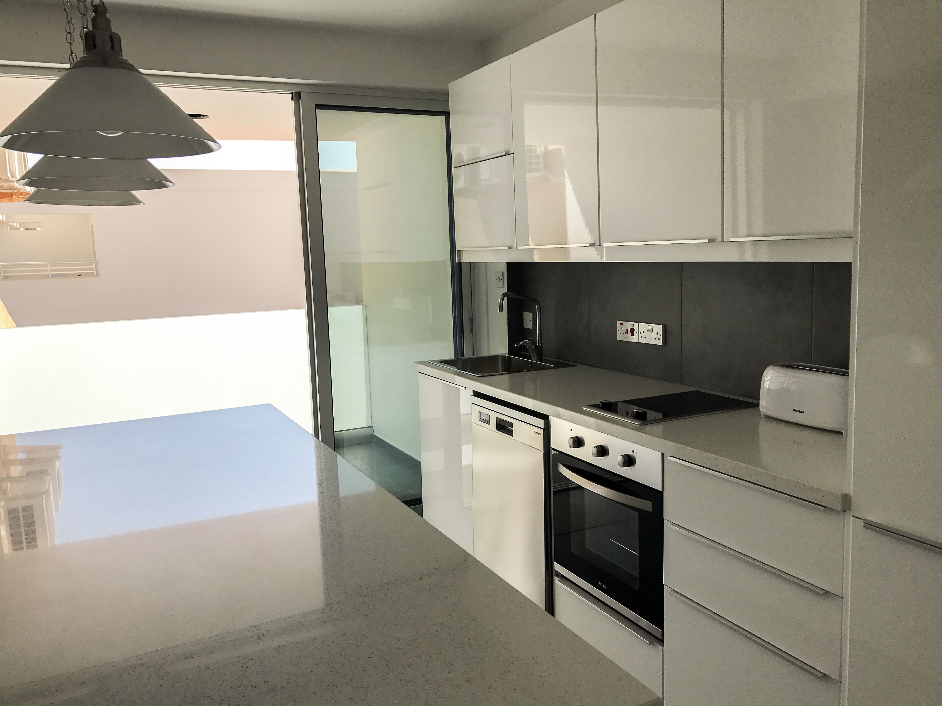 A modern kitchen with white cabinets, a stainless steel countertop, a built-in dishwasher, a stove, and a toaster.