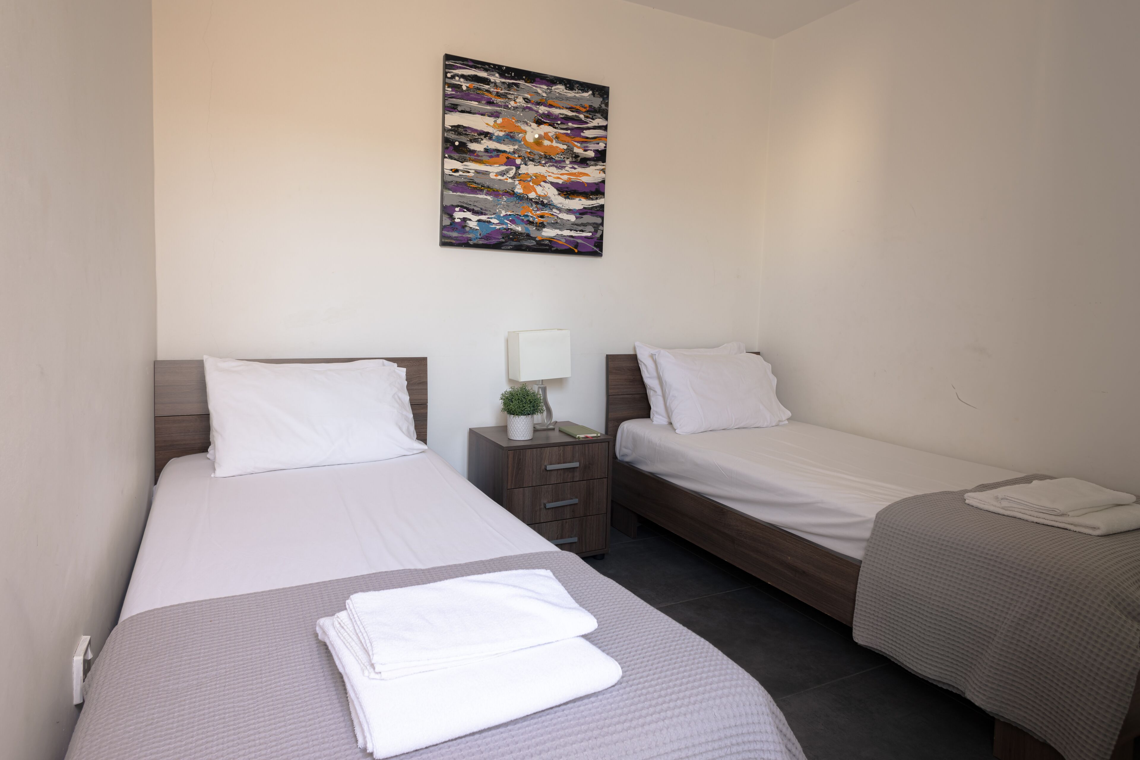 Une chambre d’hôtel avec deux lits, une table de chevet avec une lampe et un tableau au mur.