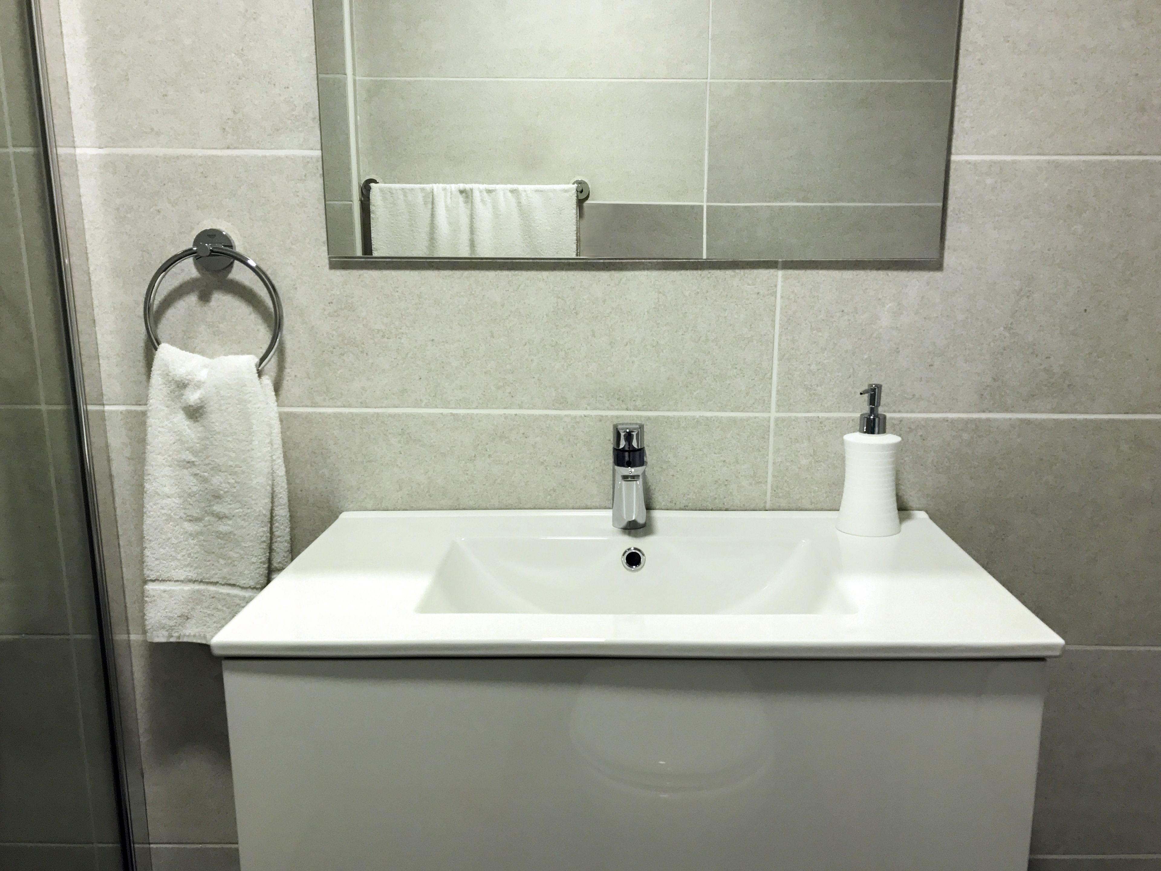 Une salle de bain avec un lavabo blanc, un miroir au-dessus et une serviette suspendue à un anneau en métal.