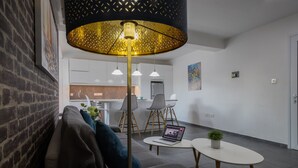 Ein modernes Wohnzimmer mit einer Couch, einem Couchtisch mit einem Laptop, einer Pendelleuchte und einer kleinen Pflanze.