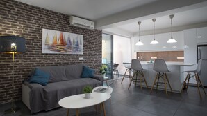 Ein modernes Wohnzimmer mit einem grauen Sofa, einem runden weißen Tisch mit einem Laptop und einem Gemälde von Segelbooten an der Ziegelwand.