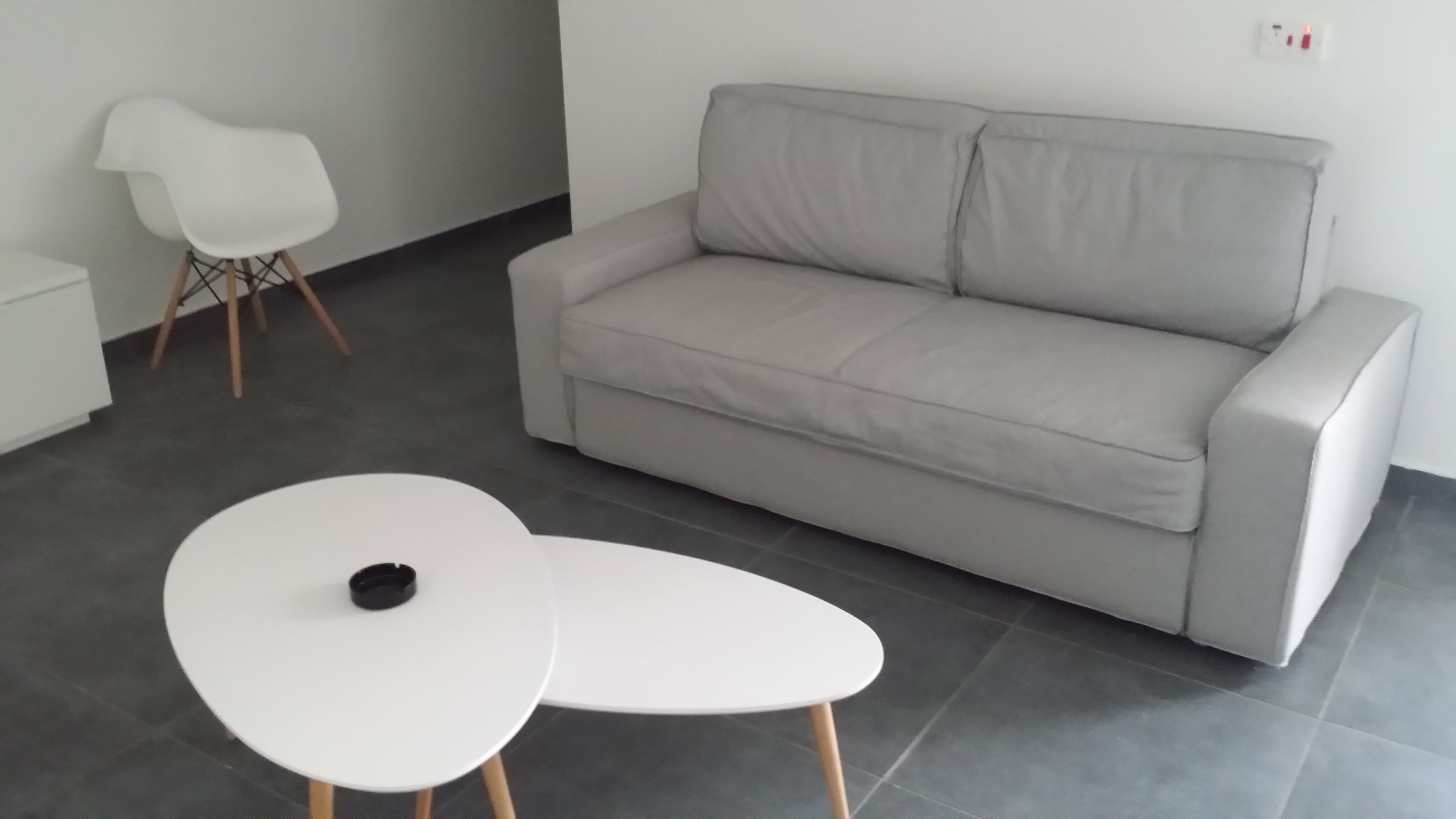 A modern living room with a grey sofa, two white tables, and a white chair.