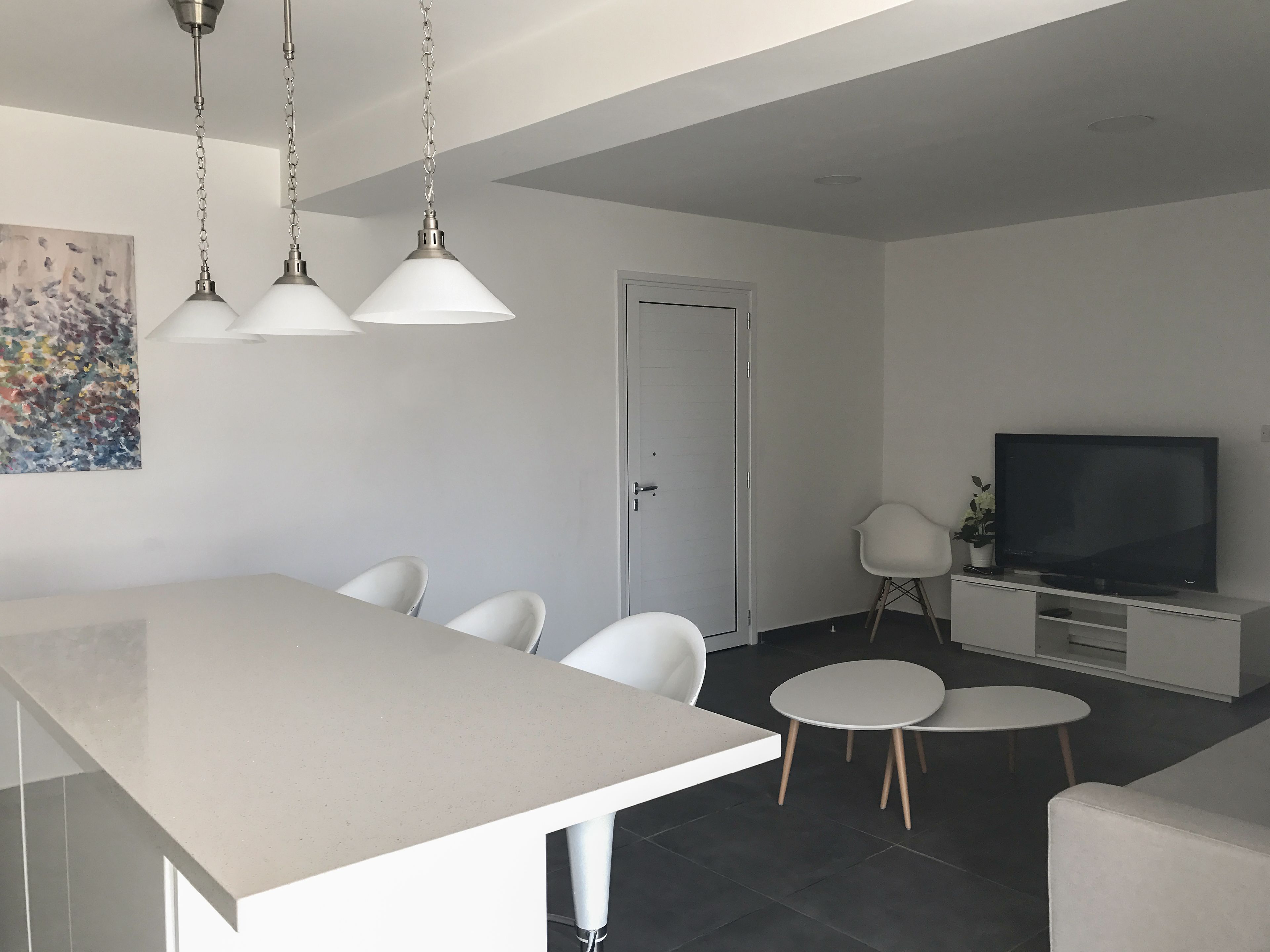 A modern living room with a dining area, a flat-screen TV, and a painting on the wall.