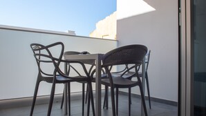 Ein Balkon mit Tisch und Stühlen, einer Glastür und freiem Blick auf den Himmel.