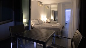 Ein Hotelzimmer mit Bett, Nachttischen, einer Lampe, einem Spiegel und einem Balkon mit Tisch und Stühlen.