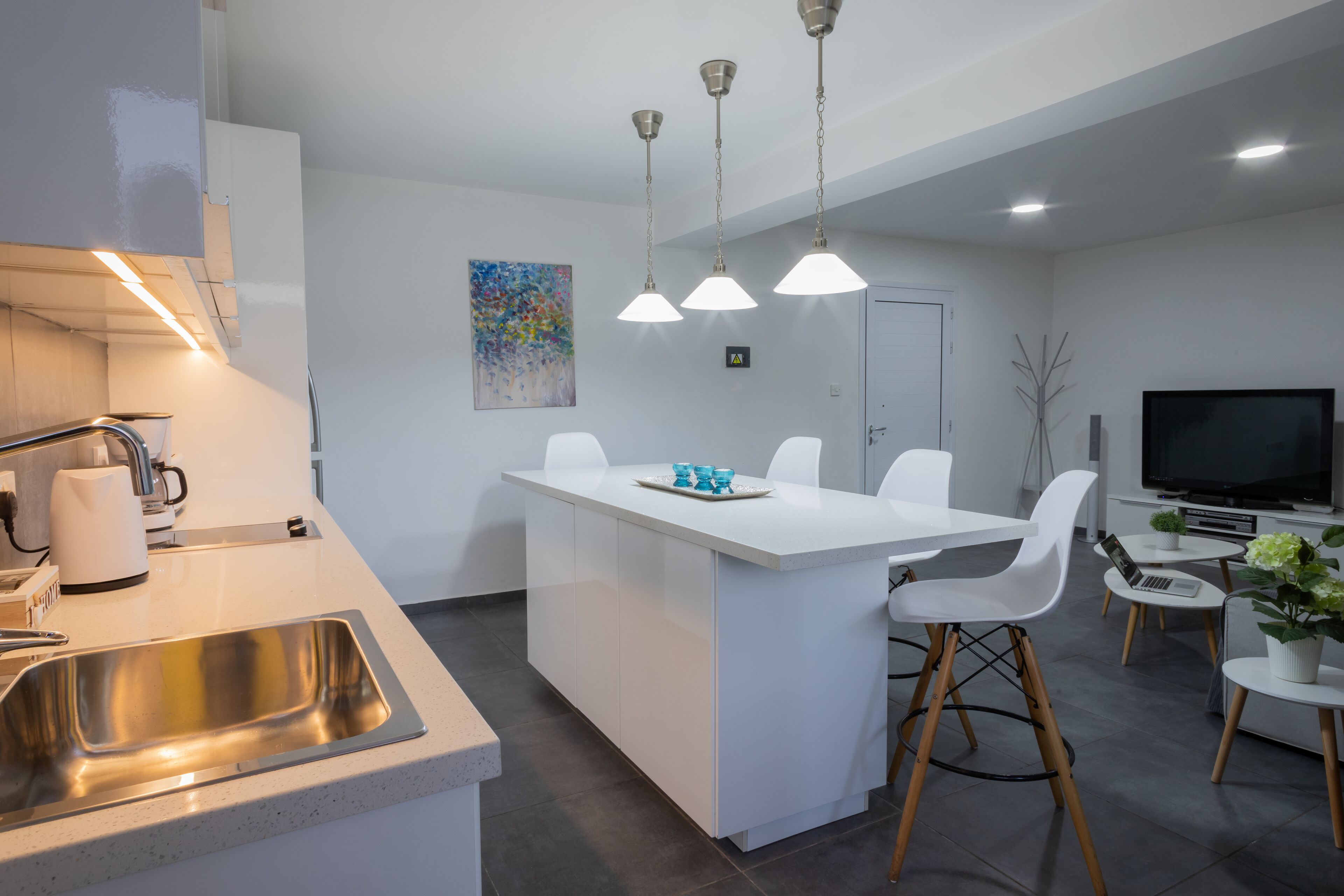 Cocina moderna con una isla central, armarios blancos, pileta de acero inoxidable e iluminación colgante.