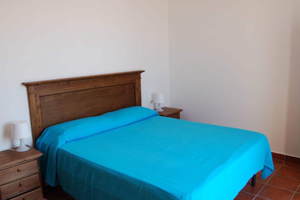Un lit simple avec une tête de lit en bois, une couvre-lit bleue et deux lampes de chevet posées sur des tables de chevet en bois.
