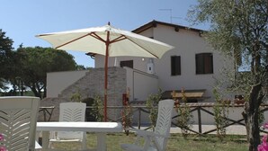 A patio with white chairs and a table, a white umbrella, and a building with a stone staircase. - Podere Valmarina (Grosseto)