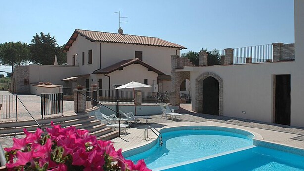 A pool area with a building, outdoor seating, and a clear sky. - Podere Valmarina (Grosseto)
