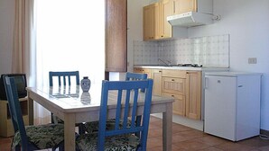 A compact kitchen with wooden cabinets, a white refrigerator, and a dining table with blue chairs. - Podere Valmarina (Grosseto)