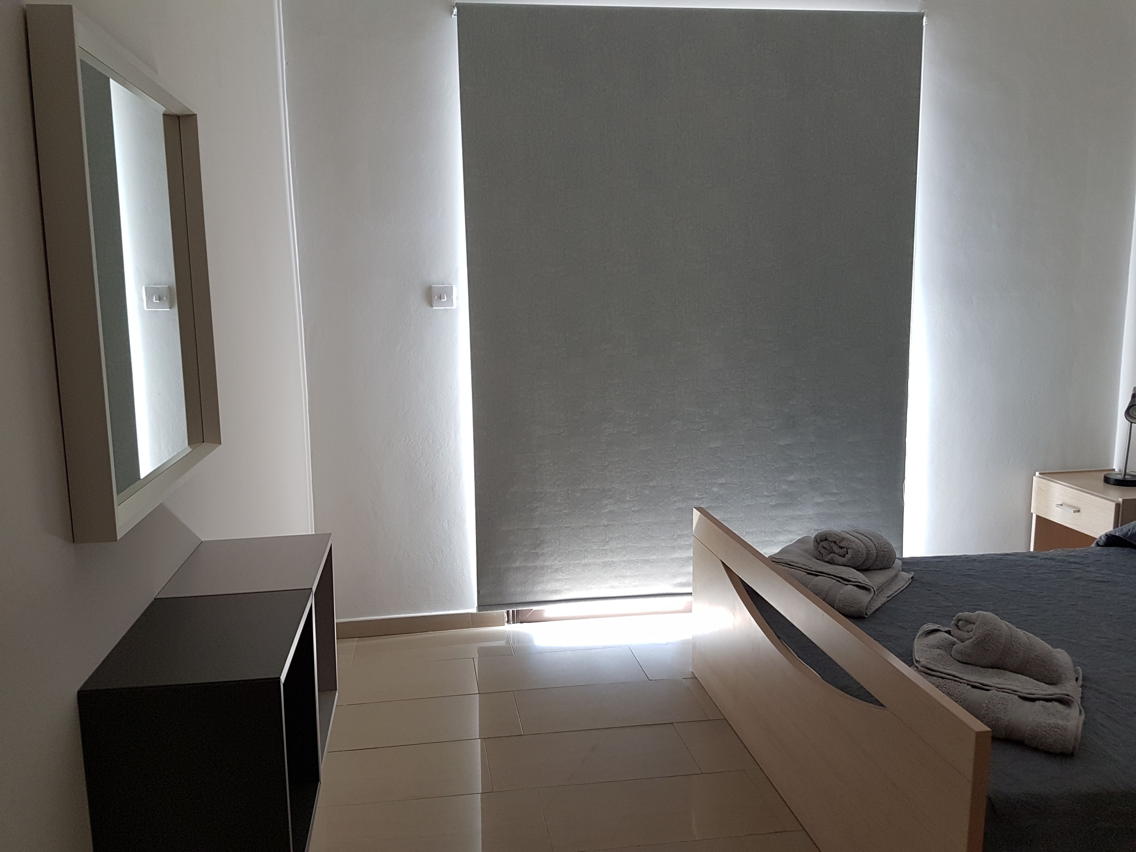 A bedroom with a bed, a bedside table, a dresser, and a mirror.
