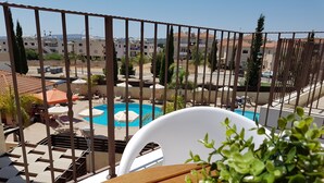 A balcony with a view of a swimming pool, lounge chairs, and a wooden table. - Marand Apartment BF11 (Paralimni)
