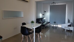 A modern living room with a dining area, featuring a sofa, chairs, a coffee table, and a TV. - Marand Apartment BF11 (Paralimni)