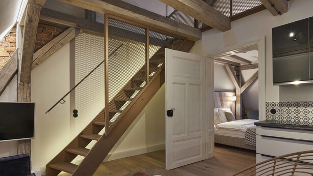 Ein modernes Schlafzimmer im Loft-Stil mit einer Holztreppe, einem Bett, einem Fernseher und einem Essbereich mit rundem Tisch und Korbstuhl.