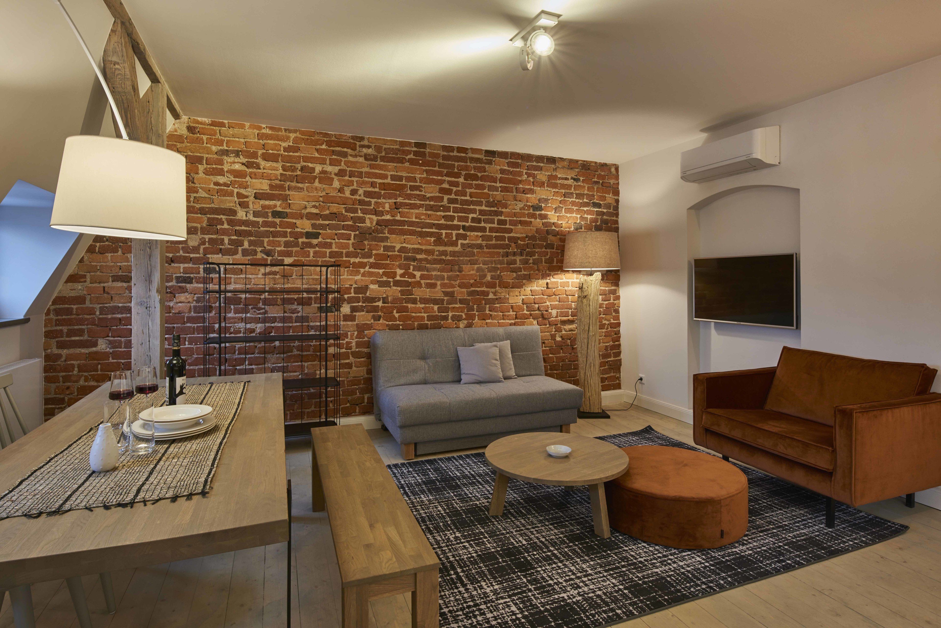A modern living room with a brick wall, a sofa, a coffee table, and a TV mounted on the wall.