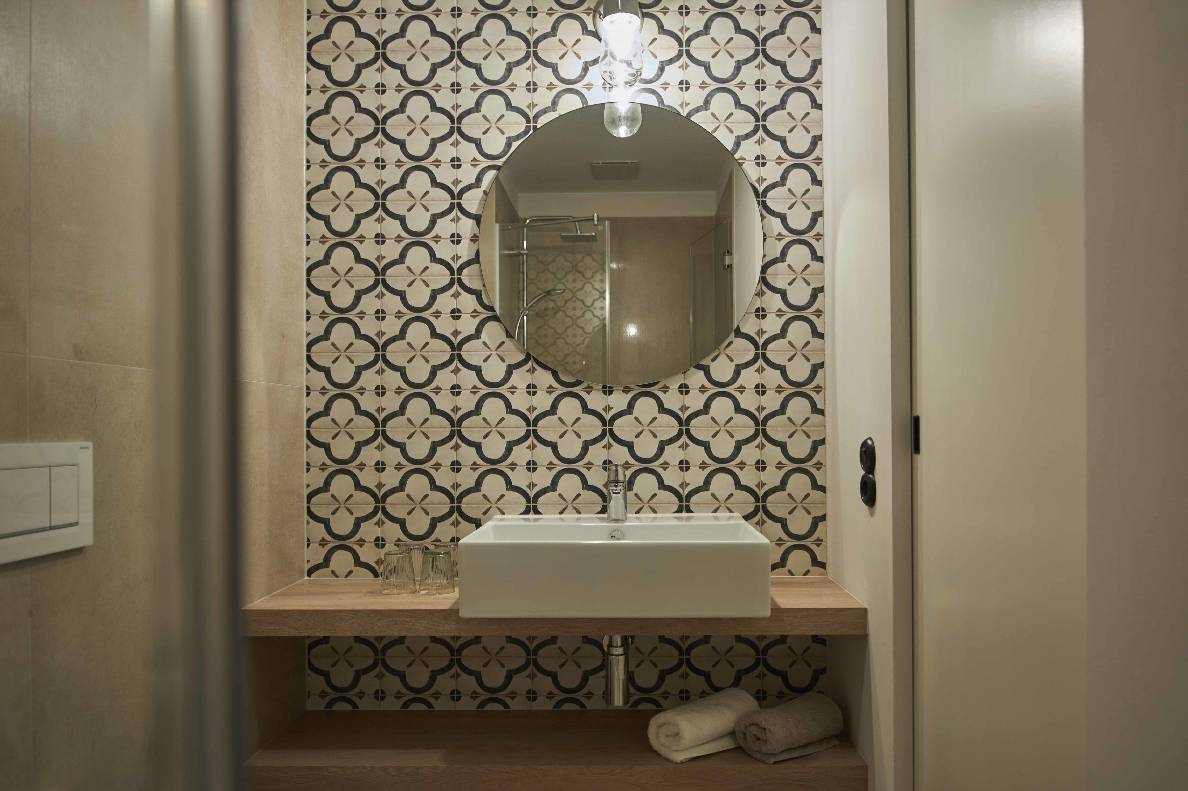 A bathroom with a rectangular sink, a mirror, and patterned tiles.