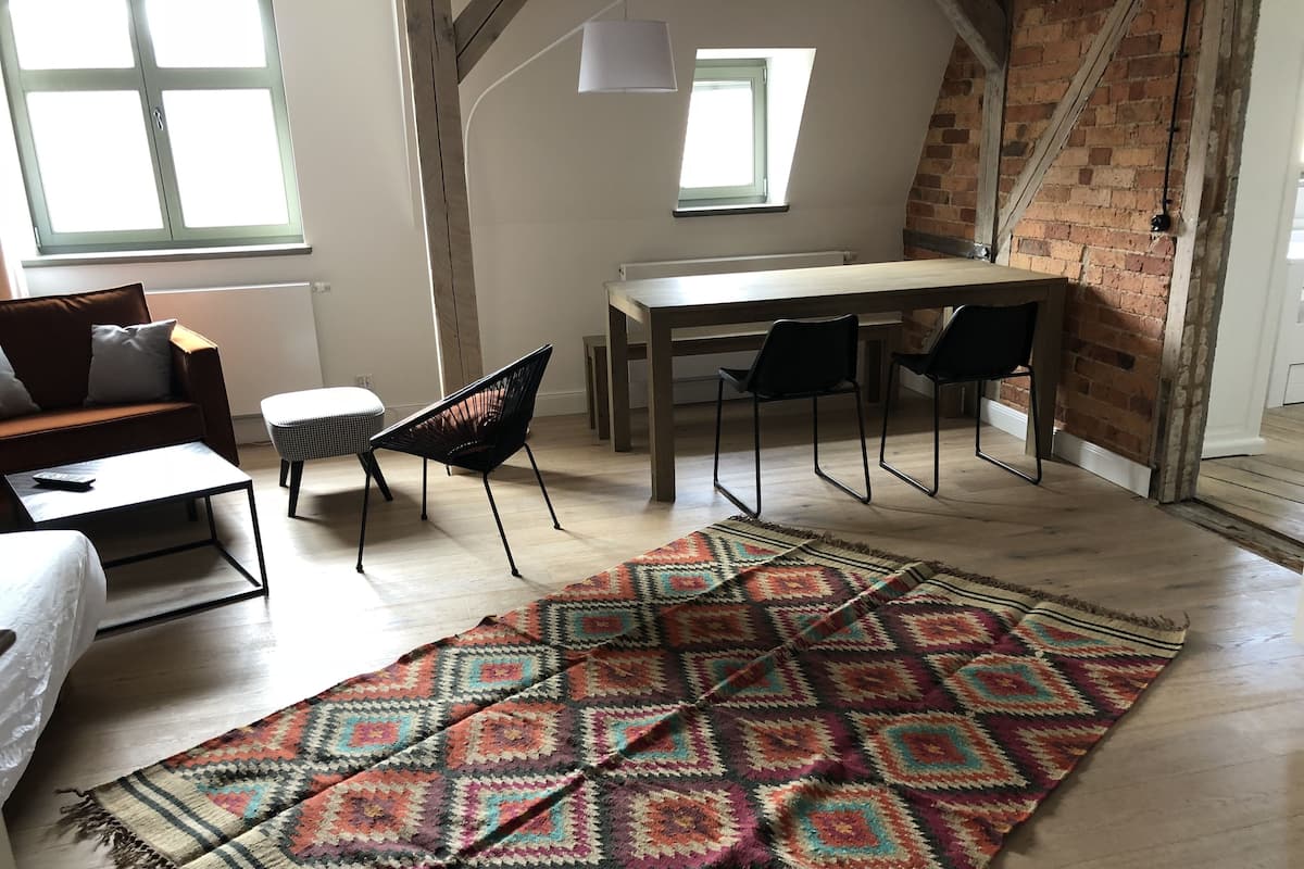 Une pièce de style loft avec une table à manger en bois, des chaises noires, un tapis à motifs, un canapé et un petit pouf.