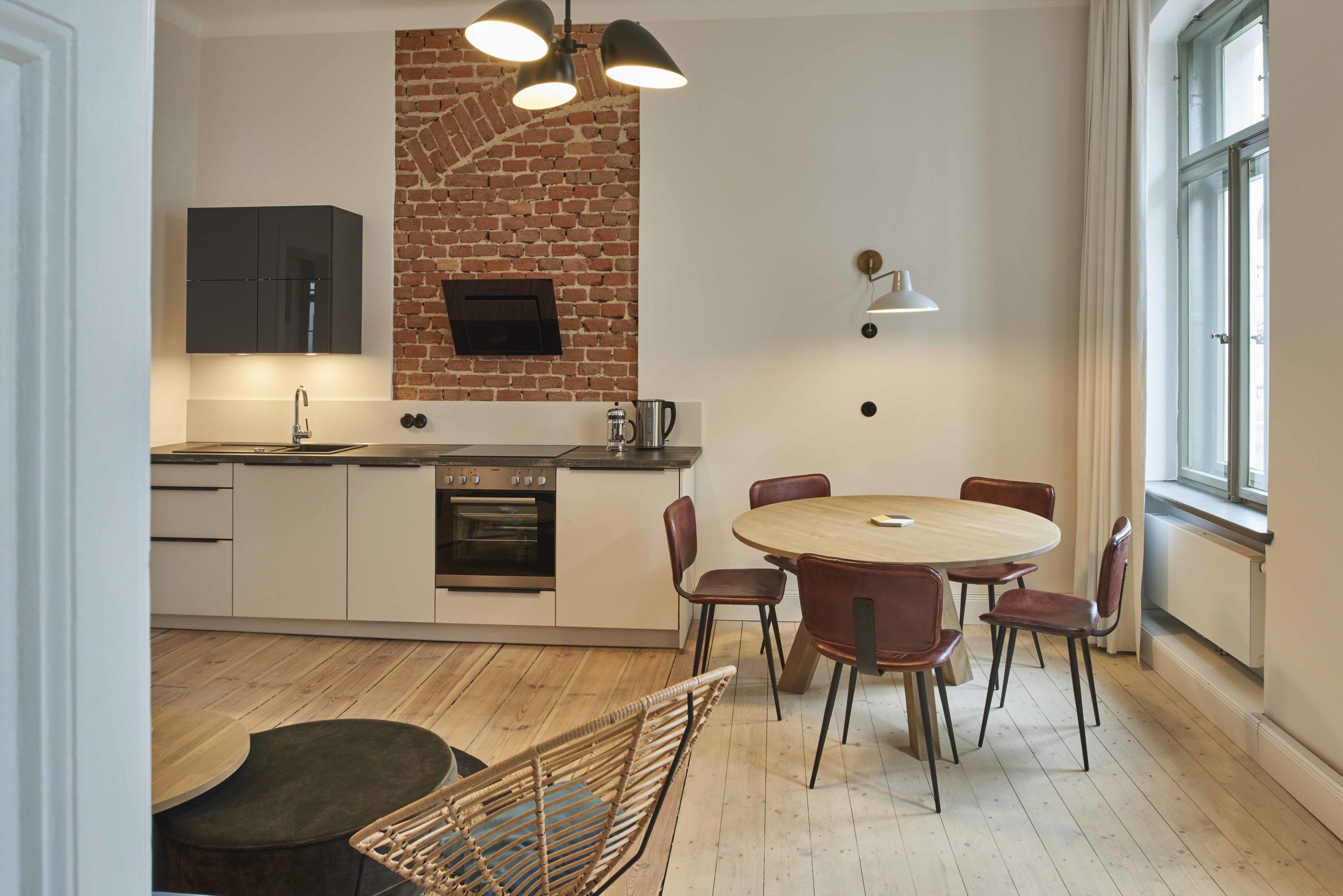 Una cocina moderna con pared de ladrillo, suelo de madera y zona de comedor con una mesa redonda y sillas.