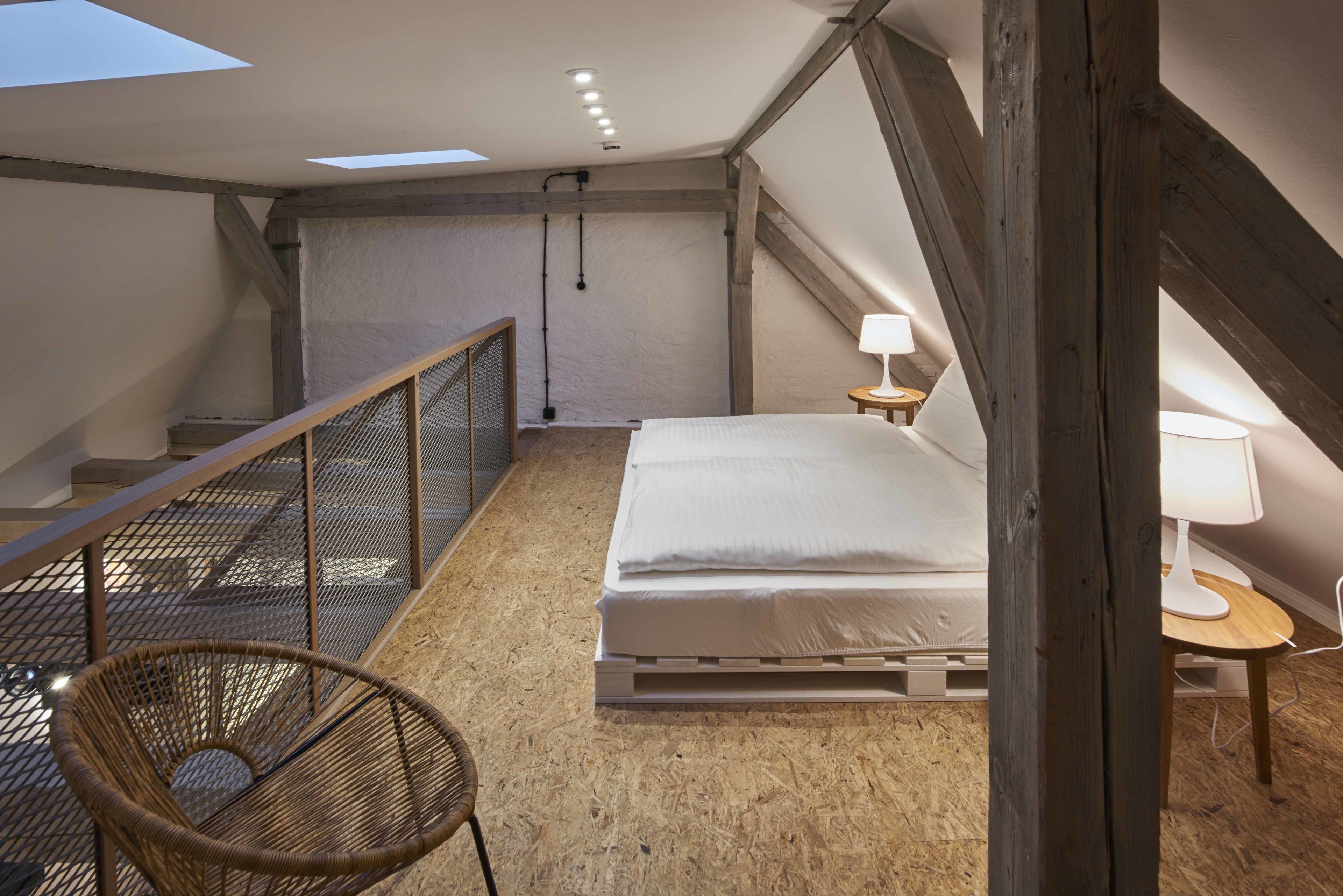A bedroom with a bed, a chair, a nightstand, a lamp, and a skylight.
