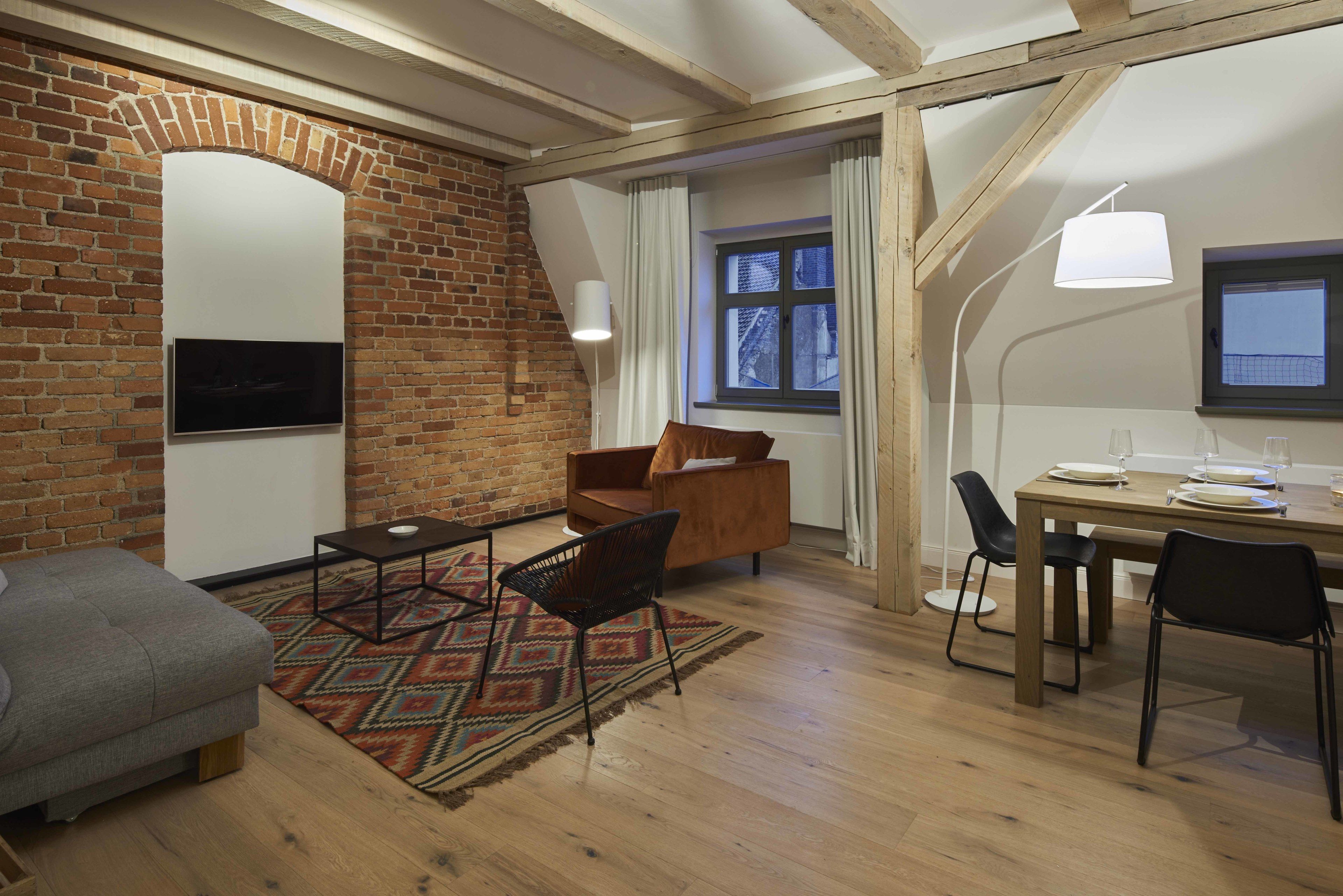 Una habitación acogedora con pared de ladrillo, televisor de pantalla plana, sofá, mesa de comedor con sillas y alfombra estampada.