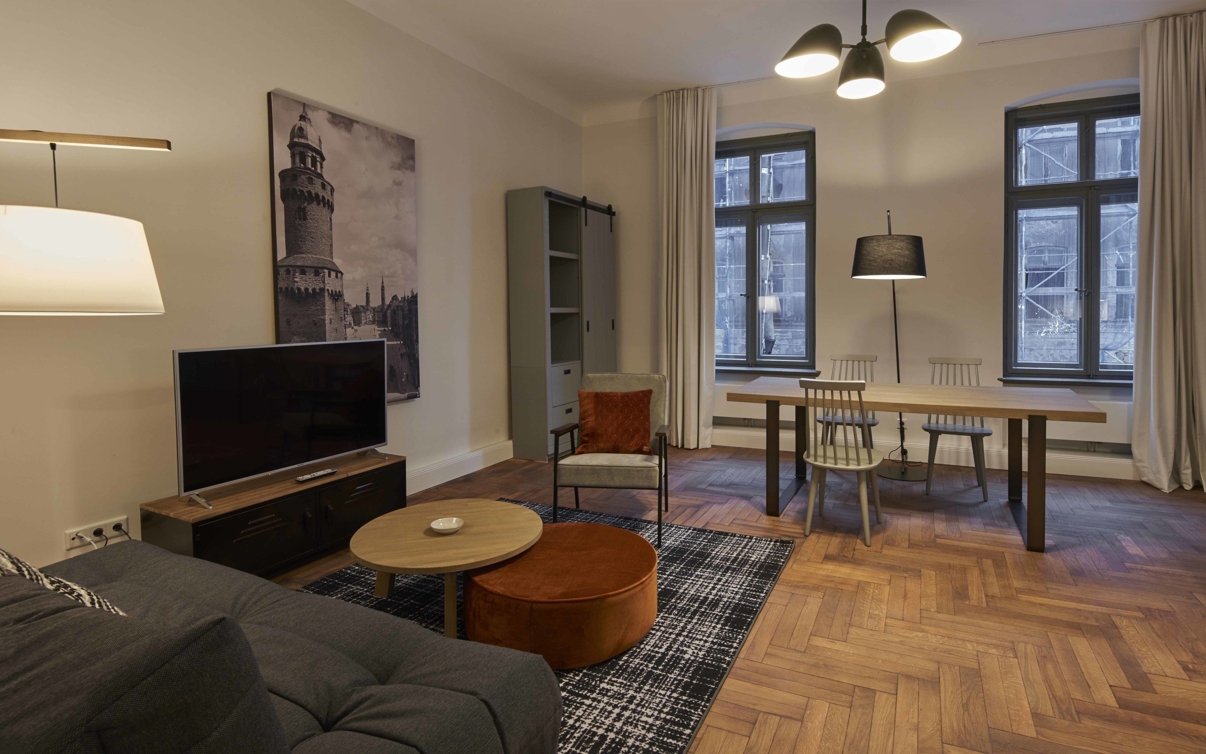 A modern living room with a flat-screen TV, a sofa, a round coffee table, and a dining area with a table and chairs.