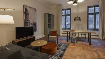 A modern living room with a flat-screen TV, a sofa, a round coffee table, and a dining area with a table and chairs.