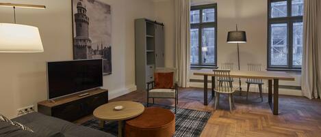 Una sala moderna con un televisor de pantalla plana, un sofá, una mesa de centro redonda y un comedor con mesa y sillas.