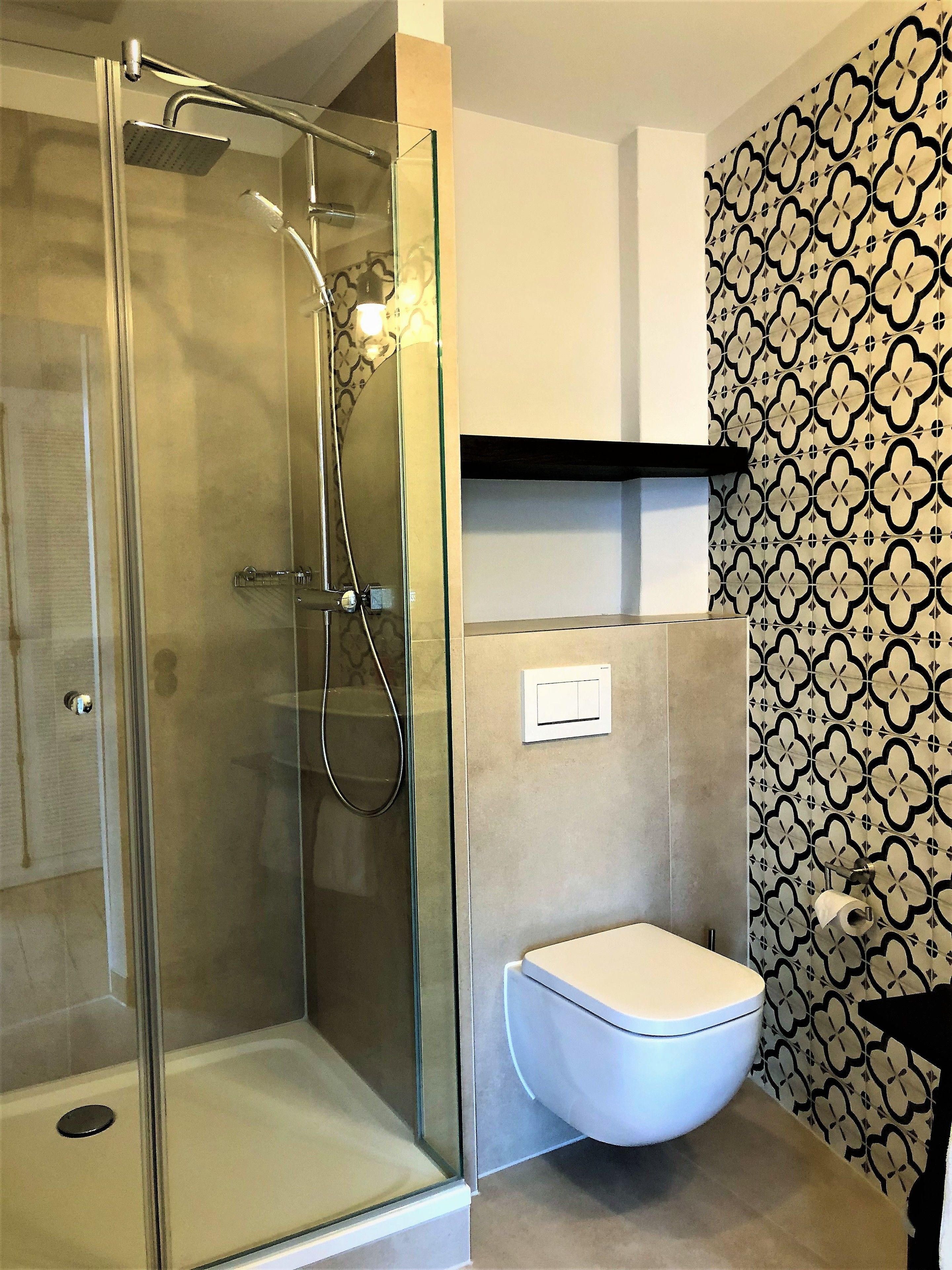 Un baño con ducha de vidrio, inodoro y pared con diseño.