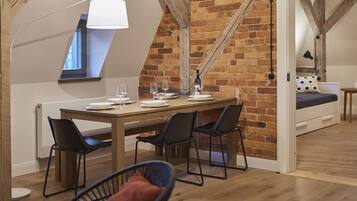 A dining area with a wooden table, four chairs, and a bench. A brick wall and wooden beams are visible in the background.