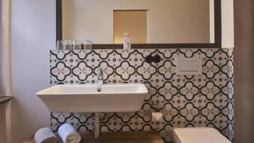 A bathroom with a white sink, a mirror above it, and patterned tiles on the wall.