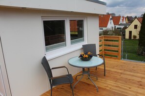 Une petite terrasse extérieure avec une table ronde et deux chaises, une fenêtre et une vue sur un quartier résidentiel.