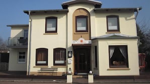 A two-story building with a central entrance, a balcony on the upper floor, and a small porch area with a bench. - Villa Wolkenlos (Dahme)