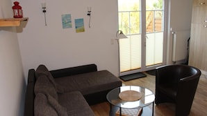 A living room with a sectional sofa, a glass coffee table, a leather armchair, and a sliding glass door leading to a patio. - Villa Wolkenlos (Dahme)