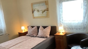 A bedroom with a bed, two bedside tables with lamps, a chair, a small table, and a wall-mounted artwork. - Villa Wolkenlos (Dahme)