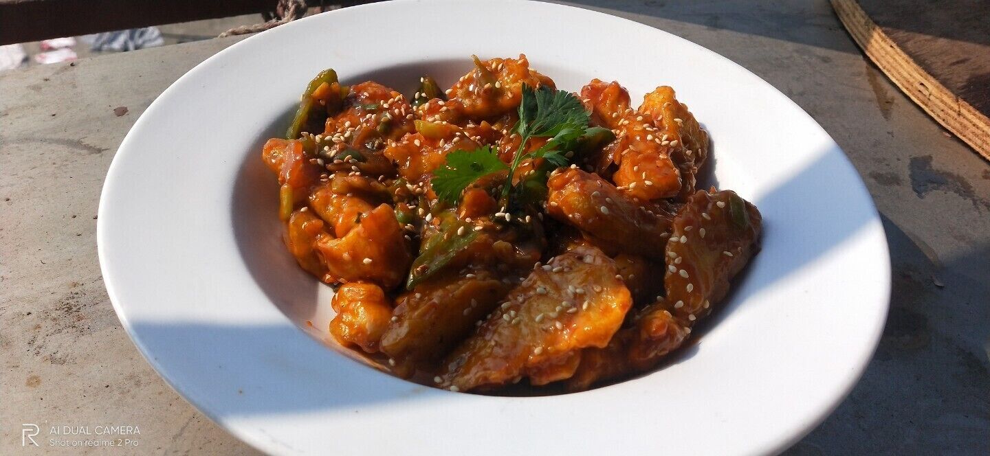 Un plato blanco con una porción de comida adornada con semillas de sésamo y una hoja, posiblemente cilantro, sobre una superficie de hormigón.