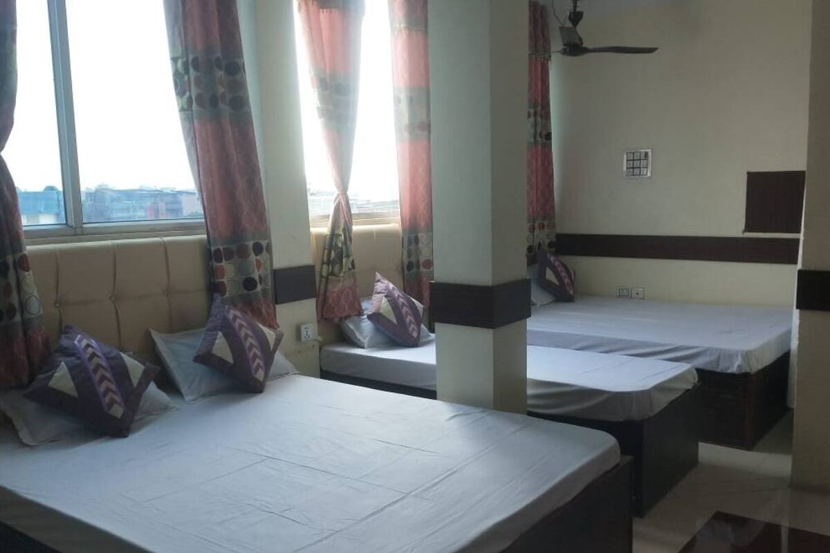 Ein Hotelzimmer mit zwei Einzelbetten, einem fensterbelaubten Fenster, einem Deckenventilator und Blick auf die Stadt.