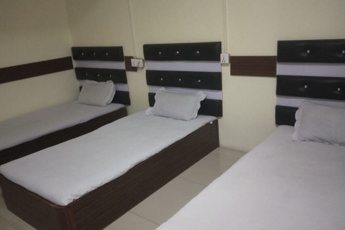 A hotel room with three single beds arranged in a row, each with a wooden headboard and white bedding.