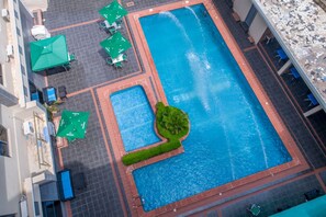 Vista aérea de una piscina con zonas de descanso y vegetación circundante.