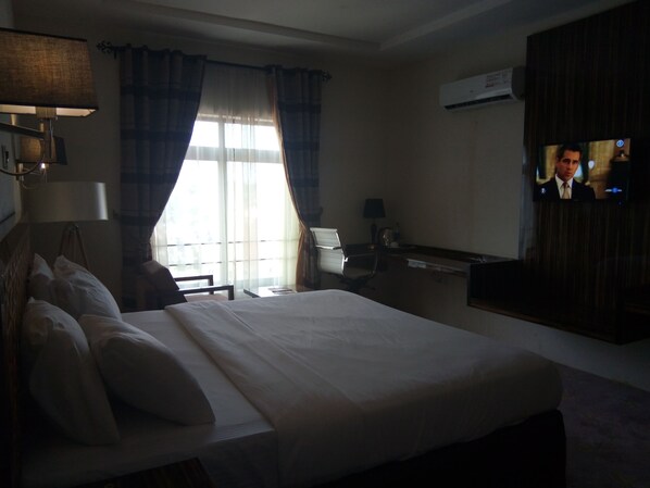 Habitación de hotel con una cama grande, un escritorio, una silla, un televisor y un aire acondicionado.