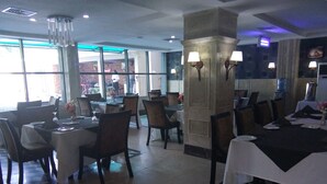 Un restaurante con mesas dispuestas para comer, suelo a cuadros y vistas al exterior a través de amplios ventanales.