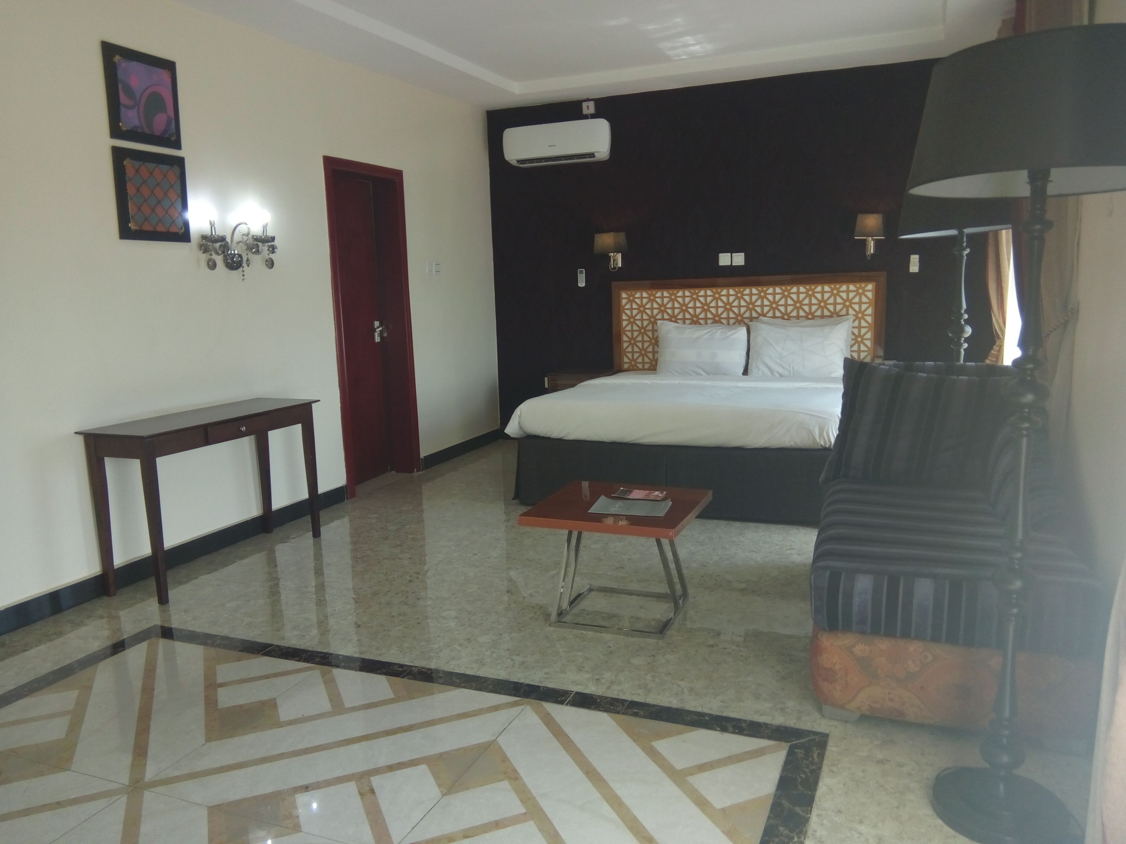 A hotel room with a bed, a small table, a sofa, a lamp, and a decorative wall piece.