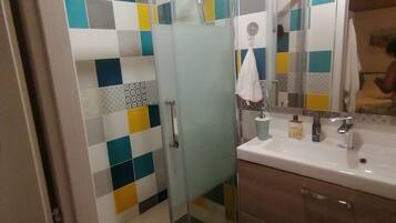 A bathroom with a glass shower enclosure, a white sink, and a mirror.