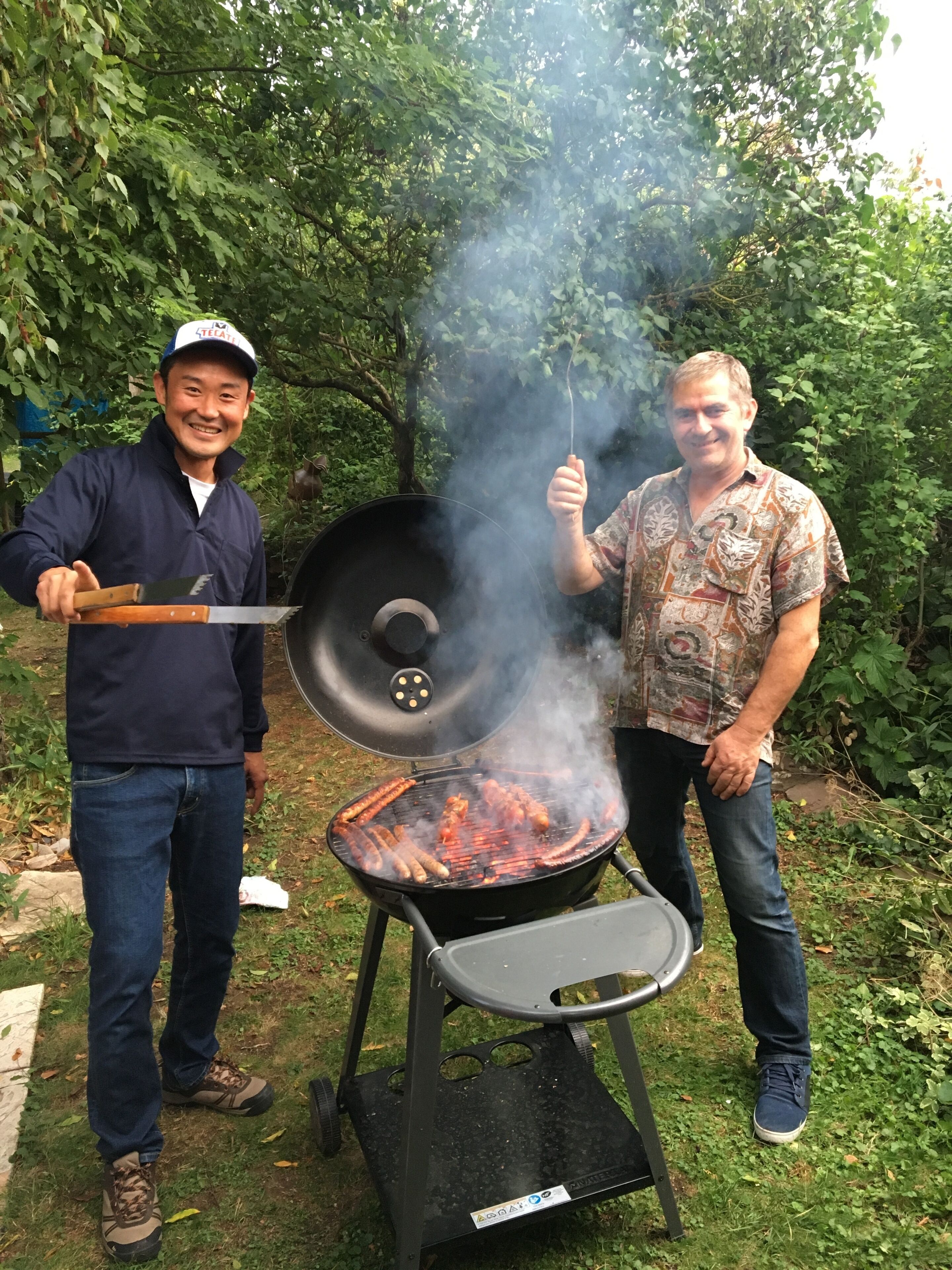 Two people grilling outdoors with a black grill in a garden setting.
