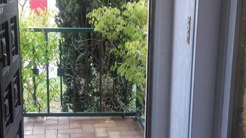 An entrance to a room with a tiled floor, a metal gate, and a view of a garden with trees and a red structure.