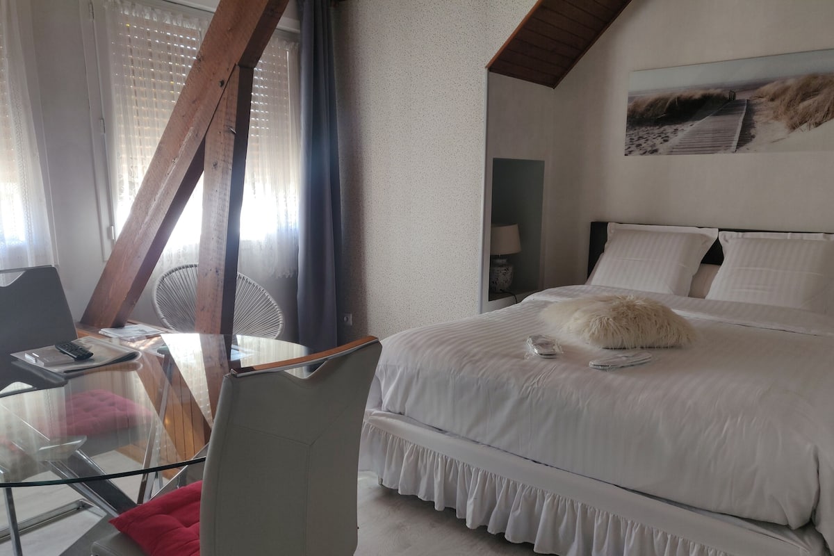 A bedroom with a bed, a desk with a chair, a window with curtains, and a wall-mounted lamp.
