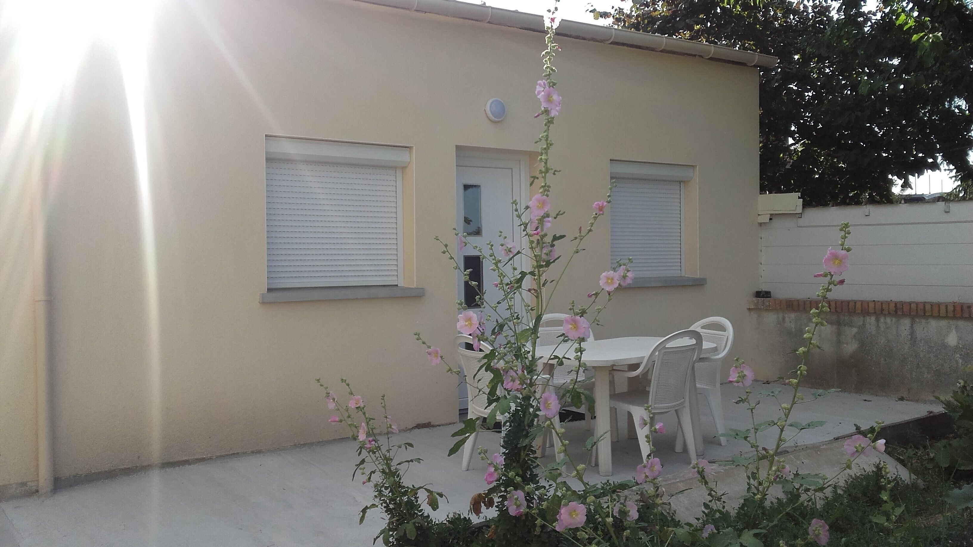 A building with two windows, a door, and a small patio area with a table and chairs.