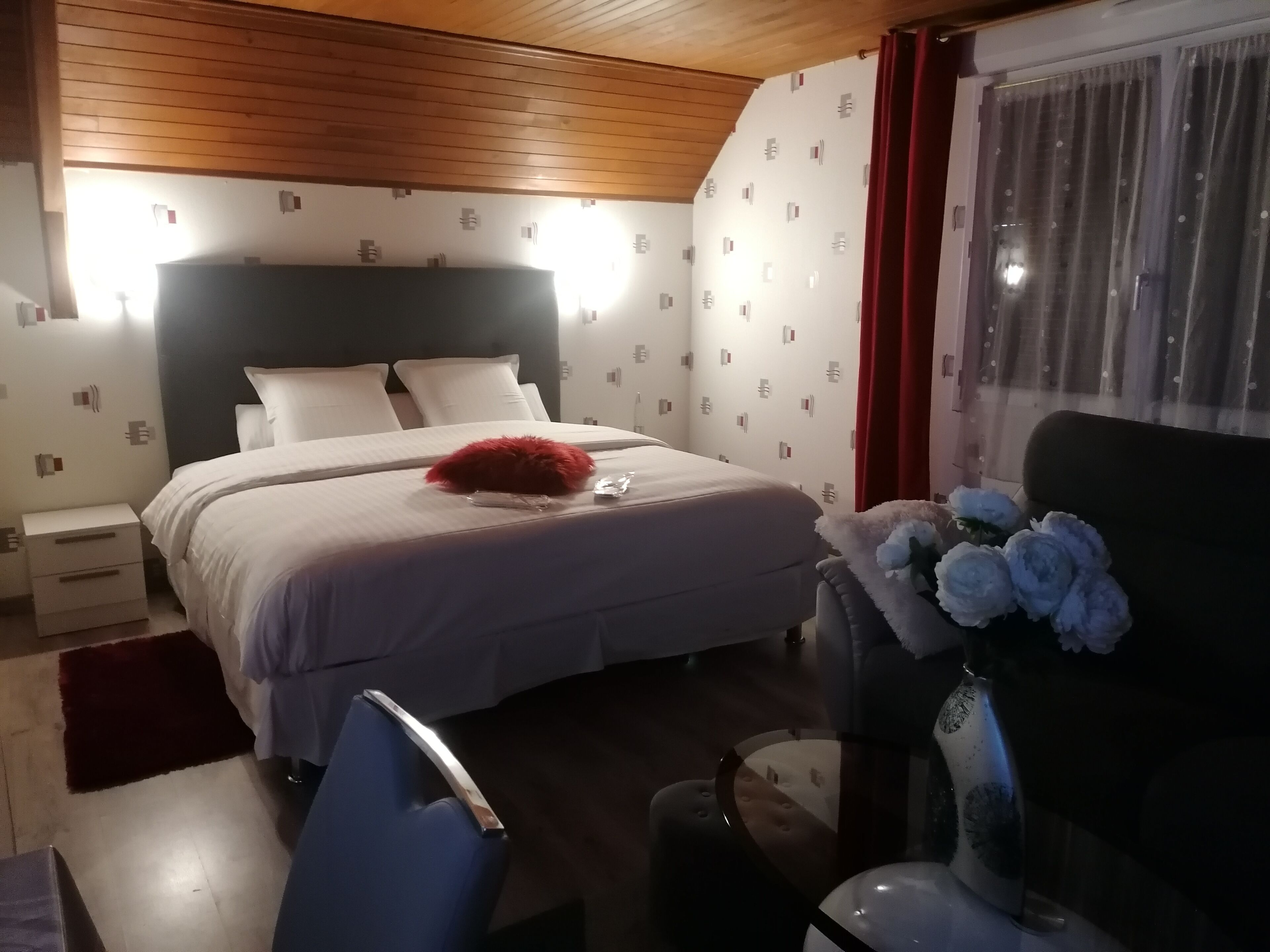 A bedroom with a bed, bedside tables, a chair, a vase with flowers, and a window with curtains.